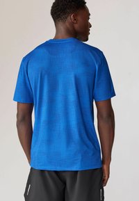 Blå kortærmet træningsshirt med et tekstureret mønster med varierende linjer. Stoffet ser let og åndbart ud.