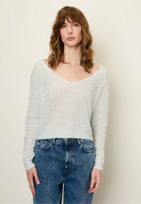 Pull long à manches longues, de couleur bleu clair et transparent, avec un large col en V et des poignets côtelés, associé à un jean en denim bleu taille haute.