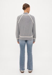 Γκρι πουλόβερ με ψηλή λαιμόκοψη, κρεμ λεπτομέρειες και ραγλαν μανίκια. Φορεμένο πάνω από ανοιχτό μπλε flared τζιν με κλασικό φινίρισμα.