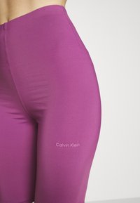 Leggings de cintura alta de Calvin Klein en un vibrante color púrpura, confeccionados con un tejido suave y elástico. Presentan un logo impreso en blanco en el muslo.