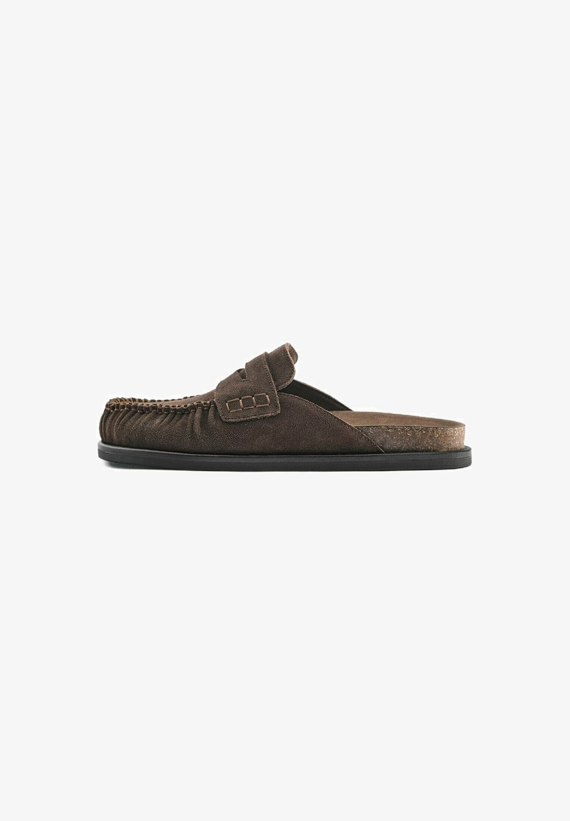 Mocassin en daim marron à enfiler avec couture style mocassin, semelle plate noire et une bride décorative sur le dessus.