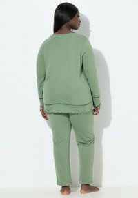 Zielony zestaw dresowy wykonany z miękkiej tkaniny, składający się z długiego topu z falowanym dołem oraz dopasowanych spodni o luźnym kroju.