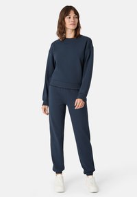 Námořnická modrá mikina a odpovídající tepláky z měkké tkaniny. Mikina má kulatý výstřih a vroubkovaný lem; tepláky mají elastické manžety.