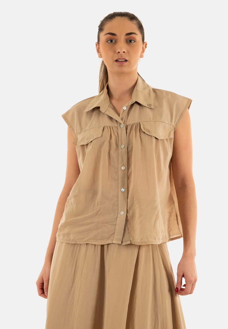 Camisa sin mangas beige, con botones y cuello, con bolsillos frontales y detalle de fruncido. Fabricada en una tela ligera y texturada.