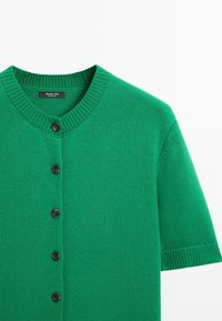 Cardigan court vert en tricot à manches courtes avec des boutons noirs sur le devant, col rond côtelé et poignets côtelés.