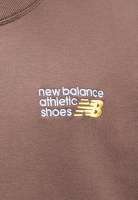 Καφέ ύφασμα με κεντημένο το κείμενο «new balance athletic shoes» σε λευκό, με κίτρινο διακοσμητικό στοιχείο σε στρογγυλή λαιμόκοψη.
