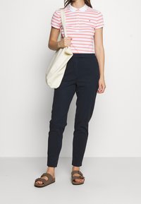 Pruhovaný růžový a bílý polo trikotu s límečkem, námořnické kalhoty a hnědé sandály. Model drží béžovou kabelku. Ležérní outfit.