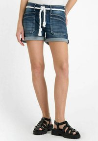 Shorts en denim avec un ourlet retroussé, des détails effilochés et une ceinture en corde blanche. Associés à des sandales noires à lanières avec une semelle épaisse.