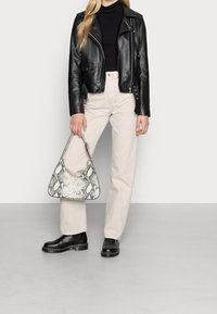 Chaqueta de motociclista de cuero negro, blusa negra con canalé, pantalones beige de pierna ancha, botines negros y un bolso de serpiente con estampado.