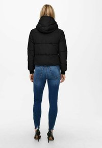 Sort puffjakke med hætte, med en quiltet design og elastiske manchetter, båret over blå denim skinny jeans.