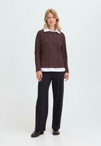 Pleteni pulover v temno rjavi barvi z teksturiranimi kabelskimi vzorci, v kombinaciji z belo srajco s kragnico in črnimi širokimi hlačami. Gladek zaključek.