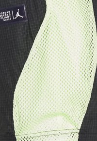 Svart och ljusgrön nätväv med ett rutmönster. Inkluderar en etikett med "Jordan Engineered Flight SU/21"-logotyp.