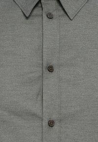 Cămașă gri cu nasturi, având un material texturat, guler clasic și nasturi întunecați cu cusături vizibile pe placket.
