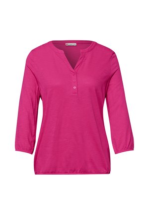 Jasnoróżowa damska bluzka z długim rękawem, z trzema guzikami na dekolcie w szpic i elastycznymi mankietami na rękawach.