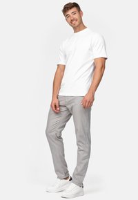 Camiseta blanca de manga corta, pantalones ajustados grises y zapatillas blancas con detalles en negro, llevadas por un hombre de pie de manera casual.