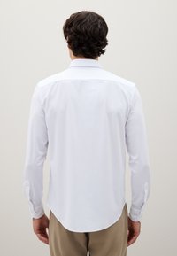 Camisa blanca de vestir de manga larga con dobladillo curvado, cuello estándar y puños abotonados. La tela parece suave y ligera.