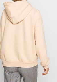 Felpa con cappuccio rosa chiaro, dal taglio rilassato, con spalle scese e polsini a costine. Tessuto morbido con una tasca a kangaroo sul davanti.