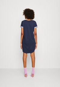 Robe T-shirt bleu marine avec des manches en denim roulées, design mi-long et coupe décontractée ; associée à des bottes à motif rose.