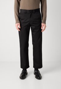 Sorte bomuldsbukser med lige ben-design, der har en knaplukning og bæltestropper. Sammen med sorte loafers.