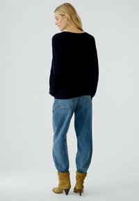 Pull en maille bleu marine foncé, jean décontracté bleu clair, et bottines beige à talons inclinés avec bouts pointus. Vue de l'arrière.