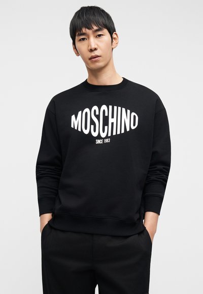 Μαύρο φούτερ Moschino με στρογγυλή λαιμόκοψη και μακριά μανίκια, με έντονο λευκό γραφικό κείμενο και λεπτομέρεια "Since 1983" κάτω από αυτό.