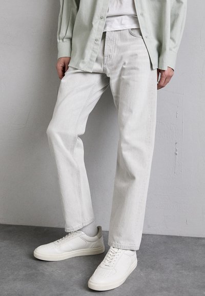 Jeans dritti grigi chiari realizzati in denim, abbinati a sneakers bianche. L'outfit presenta una vestibilità rilassata e un design minimalista.