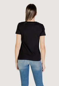 T-shirt nera a maniche corte, realizzata in cotone, con collo rotondo. Abbinata a jeans skinny blu chiaro, con dettagli nelle tasche posteriori.