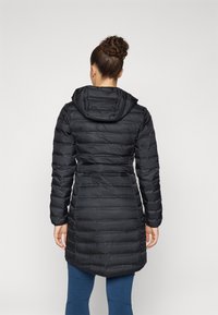 Zwarte pufferjas met capuchon, geborduurd ontwerp en een getailleerde taille voor een aansluitende pasvorm, die tot halverwege het bovenbeen reikt. Textuurstofafwerking.