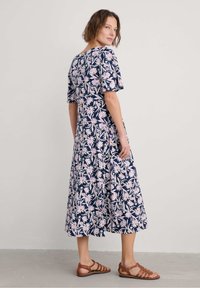 Floral print dress in navy with pink and white flowers. Short sleeves, mid-length, and flowy skirt. Brown strappy sandals complement the outfit.