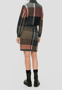 Stickad tröja och kjolset i mörkgrön, brun, rosa och beige rutigt mönster. Har ribbade ärmslut och fåll, stylar med svarta stövlar.