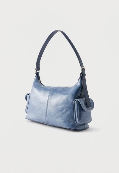 Μπλε δερμάτινη τσάντα χειρός με ρυθμιζόμενο λουρί και δύο πλαϊνές τσέπες με καπάκι σε λευκό φόντο.