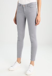 Grijze skinny jeans met een gladde textuur, vijf zakken en een knoopsluiting. Gecombineerd met witte sneakers voor een casual look.