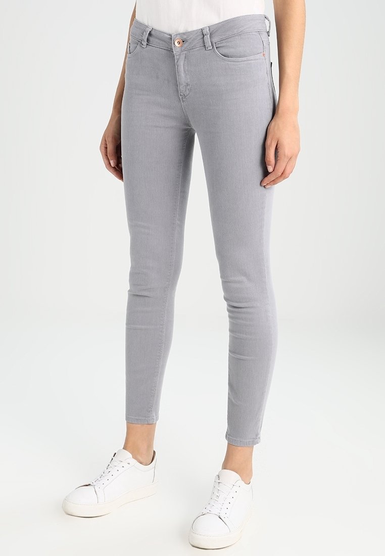 Grijze skinny jeans met een gladde textuur, vijf zakken en een knoopsluiting. Gecombineerd met witte sneakers voor een casual look.