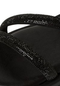 Sandalo nero con due cinturini decorati da rhinestone neri, plantare in morbido tessuto e suola liscia. Design minimalista e moderno.