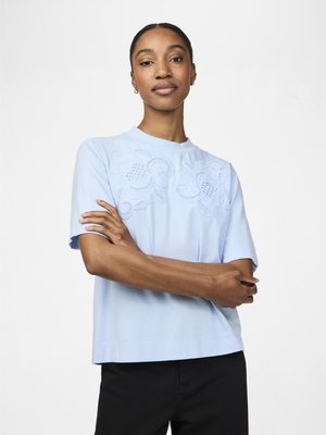 T-shirt à manches courtes bleu clair avec un élégant broderie en dentelle sur le devant et une coupe décontractée, associé à un pantalon noir.