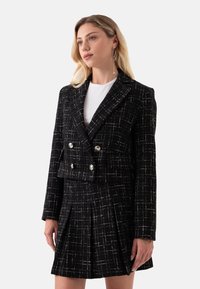 Zwart-witte geruite dubbelknoop blazer met zilveren knopen, gecombineerd met een bijpassende gepliseeerde rok, gemaakt van een textuur geweven stof.