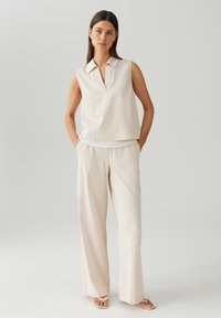 Beige mouwloos topje met kraag, gecombineerd met brede, bijpassende broek. Glad materiaal met een subtiele glans, minimalistisch ontwerp.