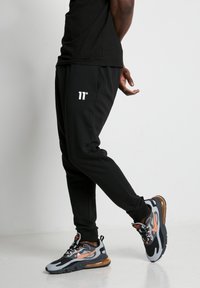 Joggers negros con logo blanco, ajuste slim, cinturilla elástica y tobillos ajustados. Zapatillas negras y grises con acentos naranjas y diseño texturizado.