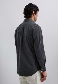 Camisa de manga larga gris oscuro con una textura suave, cuello clásico, puños abotonados y dobladillo curvado. La vista trasera muestra su diseño sencillo.