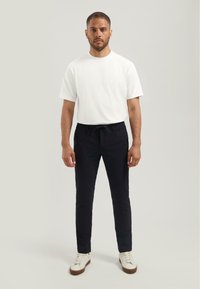 T-shirt blanche à manches courtes, pantalon de jogging noir avec une taille élastique et baskets blanches avec une semelle marron. Design simple et ajusté.