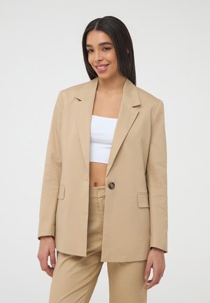 Blazer beige su misura con un solo bottone, rever a punta, due tasche frontali e maniche arrotolate, realizzato in un tessuto liscio.