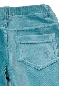 Tyrkysové kordové kalhoty s měkkou texturou, s zadní kapsou a jemným vyšitým logem. Viditelný pas a švy.