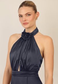 Marineblaues Satin-Halterkleid mit einem Rosendetail am Hals, gefaltetem Oberteil und einem Ausschnitt unter der Brust, das eine figurbetonte Taille hat.