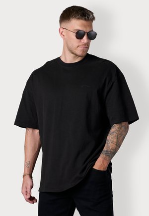Schwarzes, oversized T-Shirt mit rundem Halsausschnitt und kurzen Ärmeln. Aus Baumwolle gefertigt, mit dezenter Markenkennzeichnung und lässiger Passform.