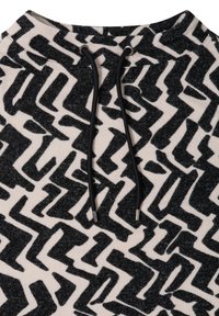 Schwarze und weiße gemusterte Kapuzenjacke mit Zickzackdesign, aus einem strukturierten Stoff gefertigt, mit einer Kordelzugvorrichtung am Halsbereich.