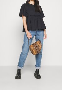 Haut noir à manches courtes avec détail à volants, associé à un jean bleu clair et des bottines noires épaisses. Tenant un sac marron à motif peau de serpent.