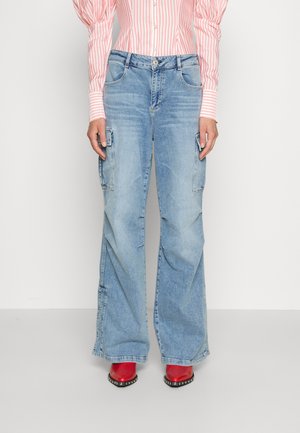 Jean cargo bleu clair à jambes larges, avec des poches plaquées de chaque côté et une fermeture classique à bouton. Associé à des chaussures à talons rouges.