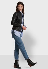 Crna kožna jakna s uskim krojem, prebačena preko plave pruge košulje. Uparena s opuštenim trapericama i crnim čizmama s potpeticom.