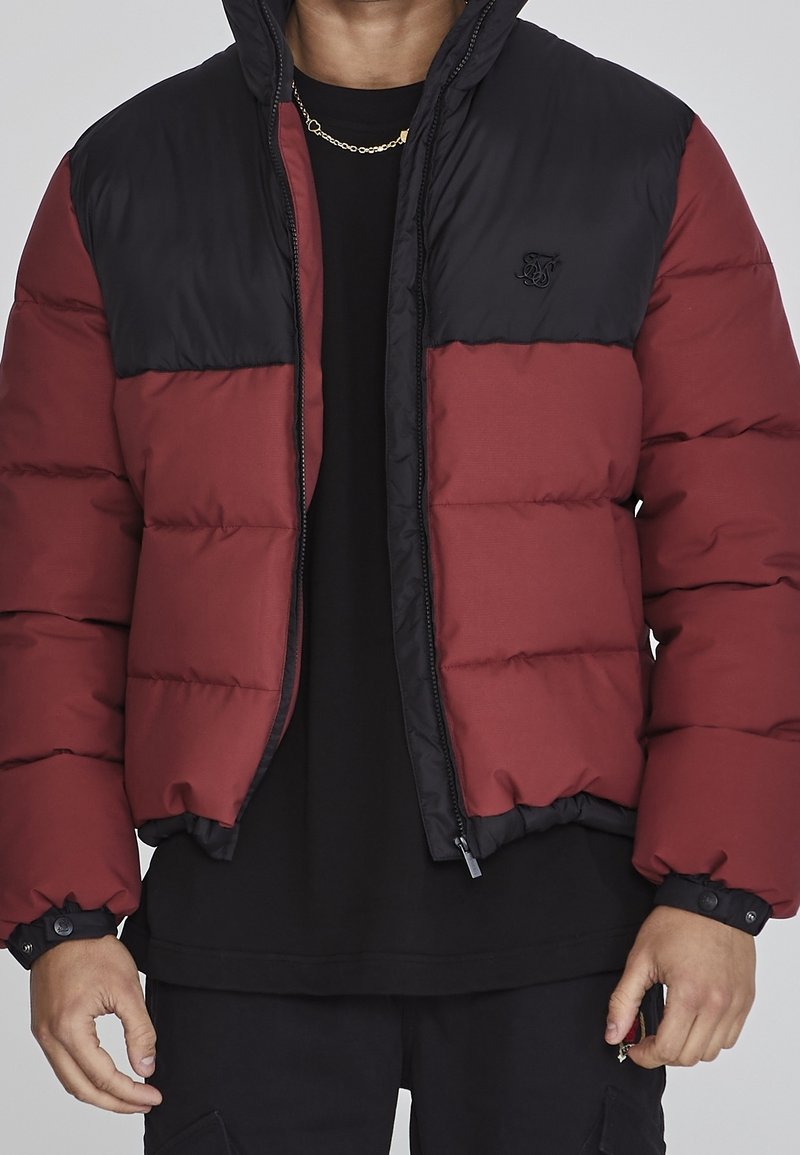 Rød og sort dunjakke med lynlås foran, let quiltet tekstur og logo på brystet. Har hætte og elastiske manchetten.