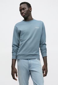 Ανοιχτό μπλε φούτερ με στρογγυλή λαιμόκοψη, με ριμπ μανσέτες και τελείωμα, με μικρό λευκό λογότυπο στο στήθος. Μαλακή υφή υφάσματος, άνετη εφαρμογή.